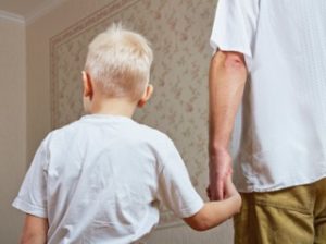 young blonde boy is led down the hall by his father