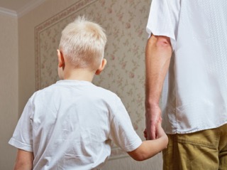 young blonde boy is led down the hall by his father